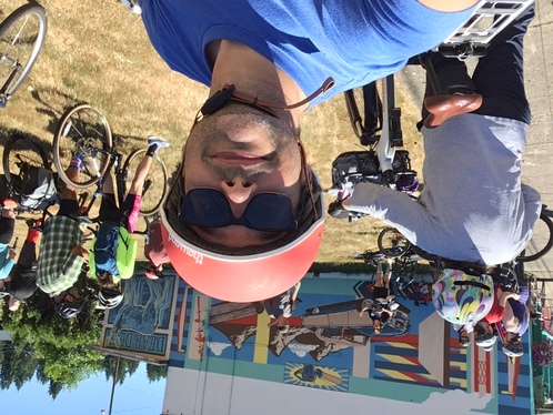 Selfie of myself with sunglasses, a red helmet in front of a group of people with bikes looking at a mural