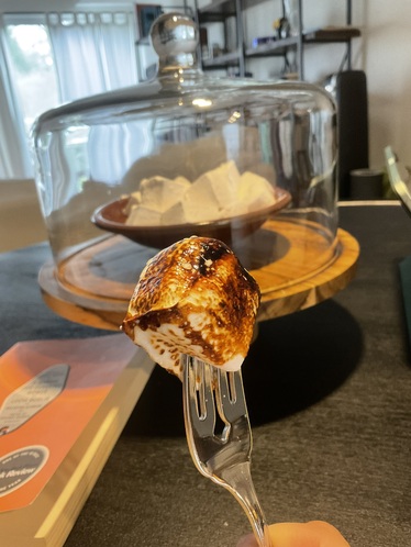 A picture of a toasted marshmallow on a fork in front of a plate of marshmallows